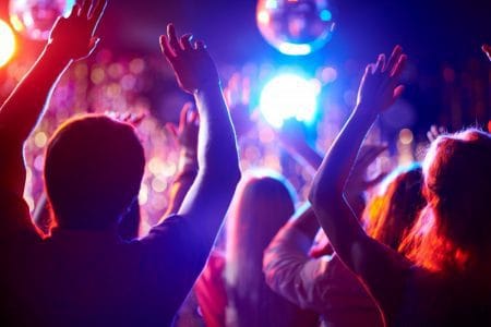 Crowd of people with raised arms dancing in night club