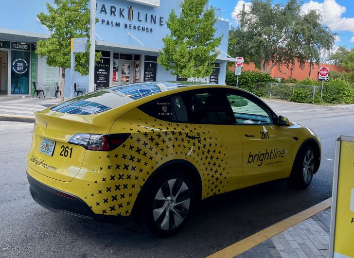 Bright yellow Telsa parked in from of a Brightline station.