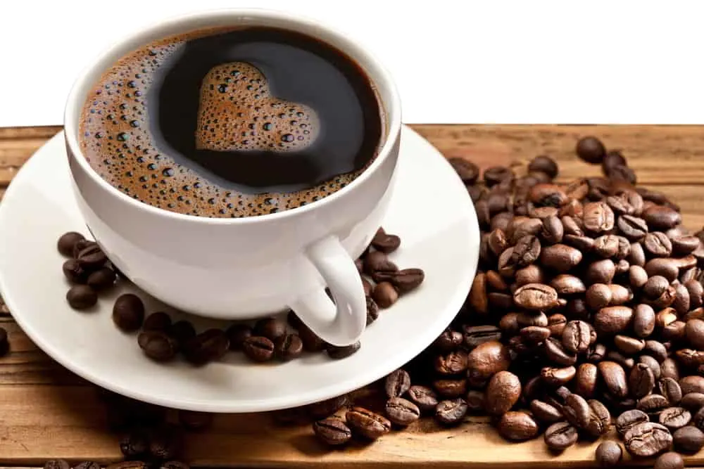 A cup of black coffee in a white cup on a saucer, surrounded by coffee beans.