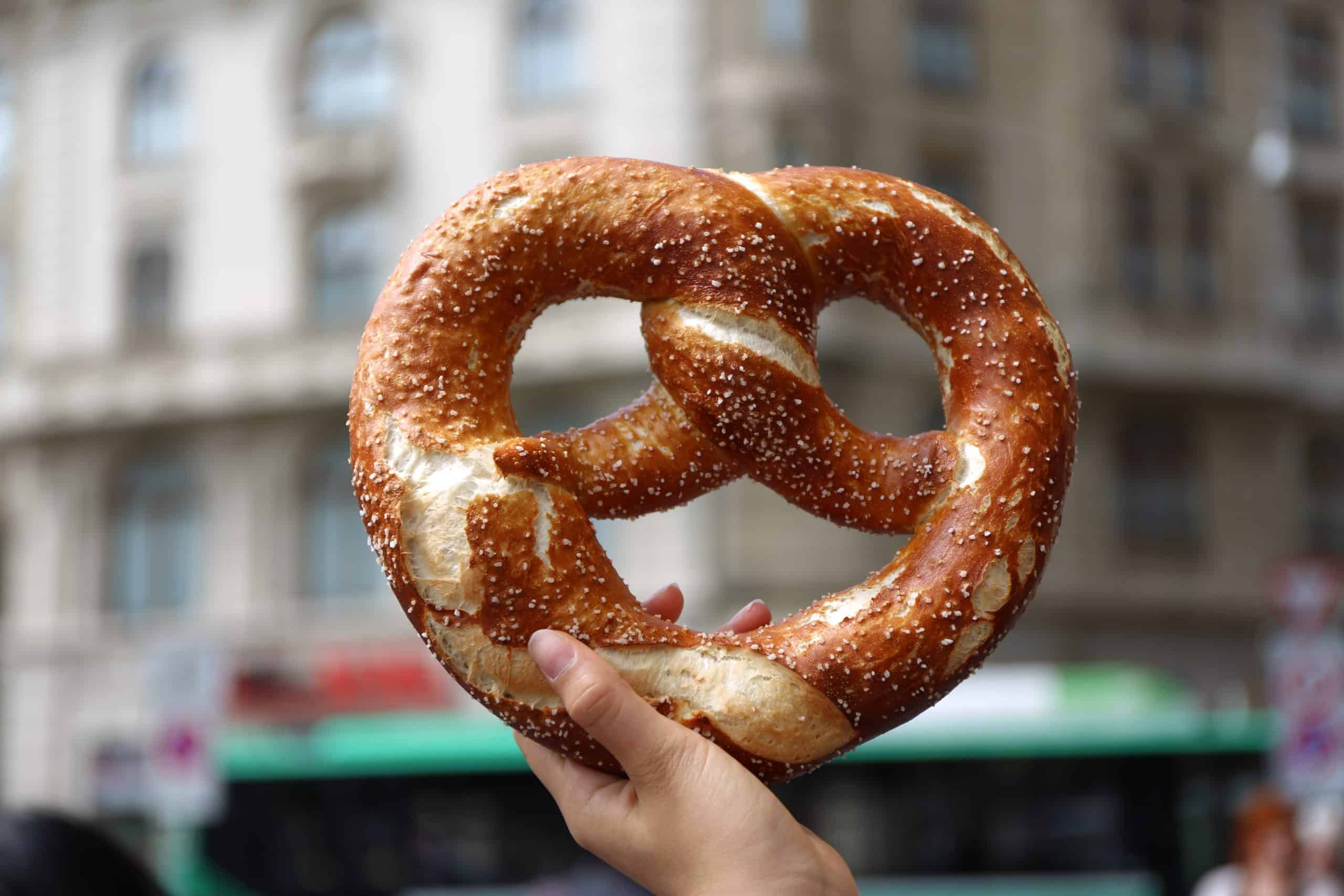 National Pretzel Day Deals - hand holding up a soft pretzel against an urban setting